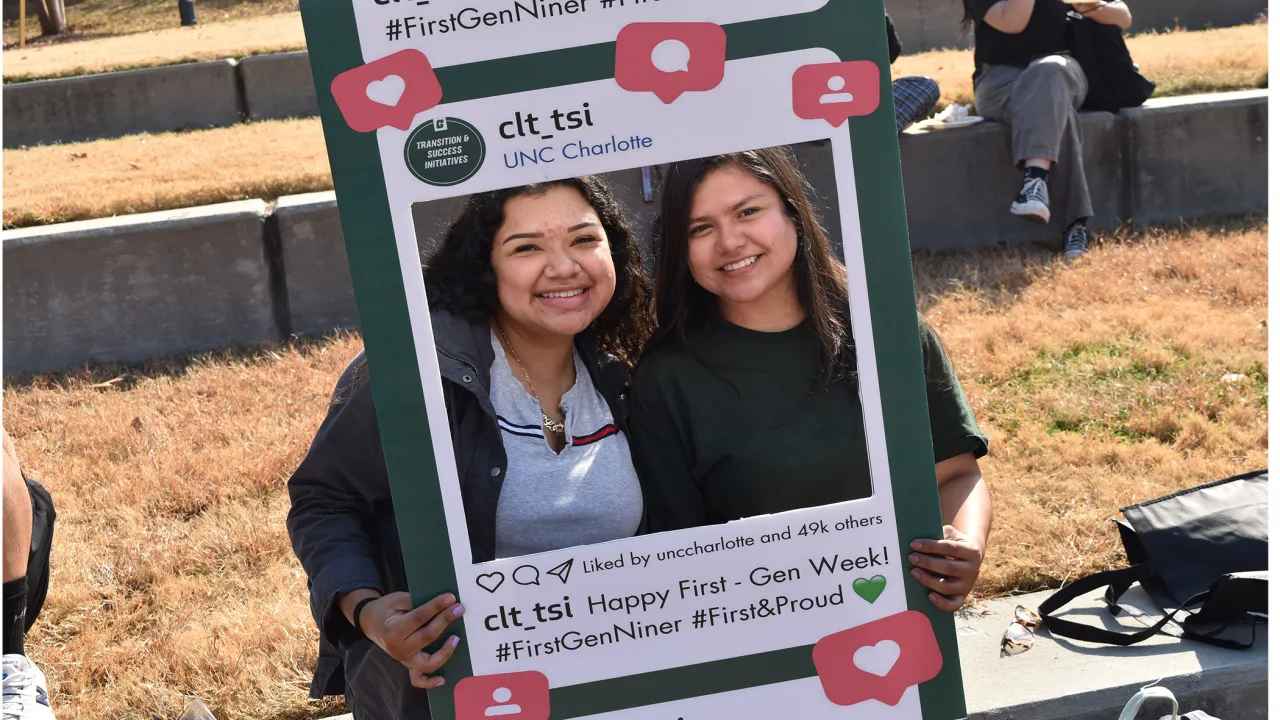 Two students holding photo frame smiling at first-gen cookout