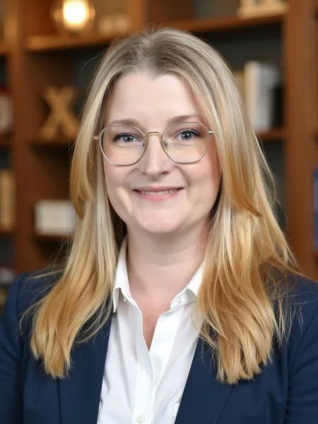blonde person wearing glasses wearing a navy blue suit and white button up