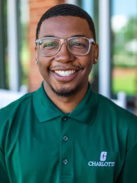 man smiling in a green polo wearing clear glasses with a blurred background