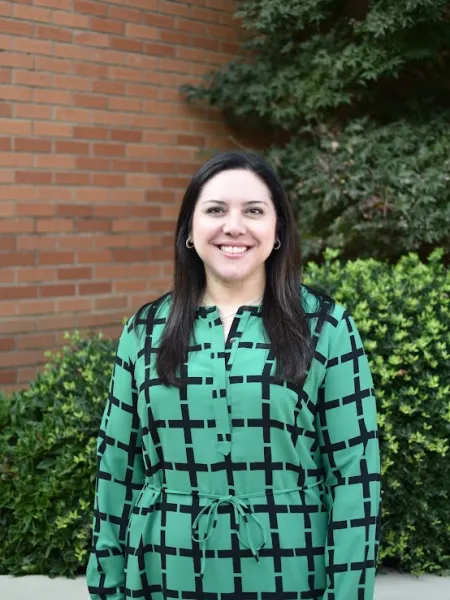 Woman facing the camera smiling with black hair and wearing a green and black shirt. 