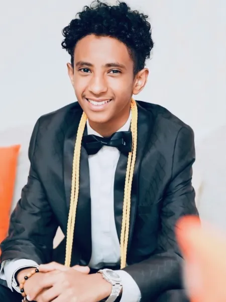 Young man with a tuxedo on and 2 gold graduation cords.