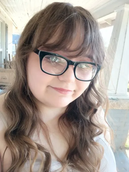 Women wearing black square glasses with wavy brown hair smiling softly at the camera