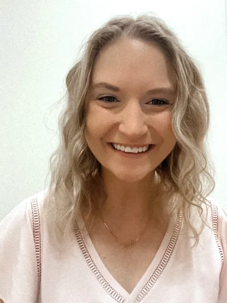 Person in pink shirt posing for headshot against a blank wall.