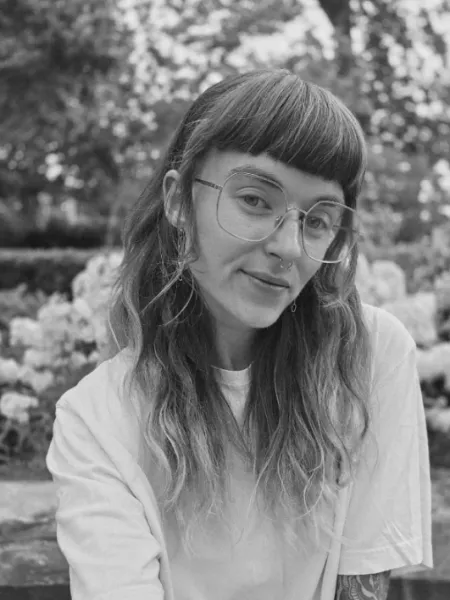 Black and white photo, person with bangs and glasses in a white t-shirt 