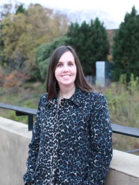person standing in front of trees in a animal print blouse, smiling