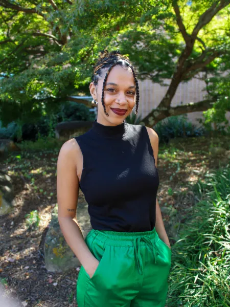 Person in black top and green pants posing for headshot.