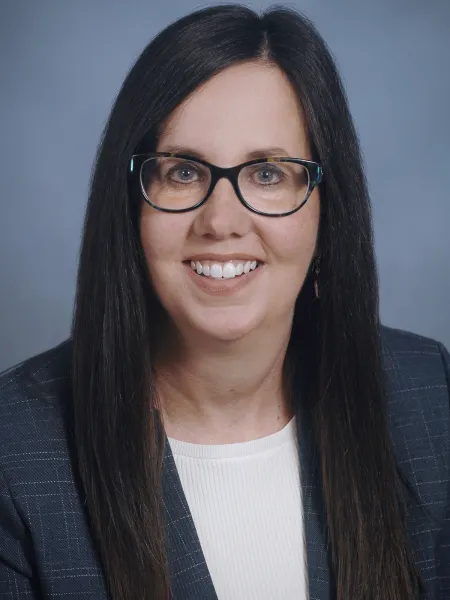 Person in blue plaid blazer and glasses posing for headshot.