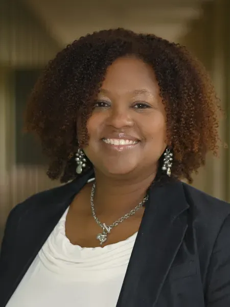 person standing in a black blazer with white blouse smiling 