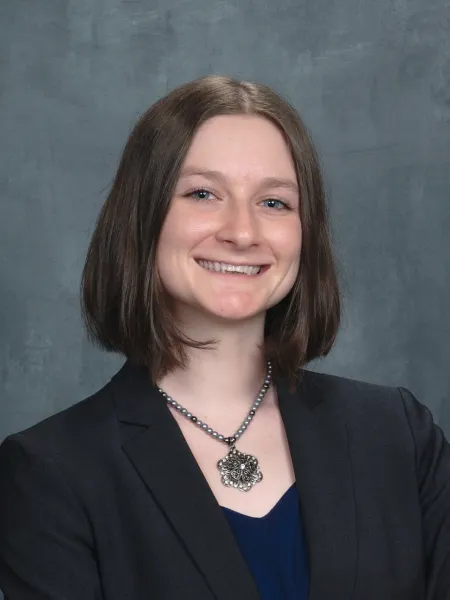 Person with short brown hair wearing a black blazer paired with a flower necklace