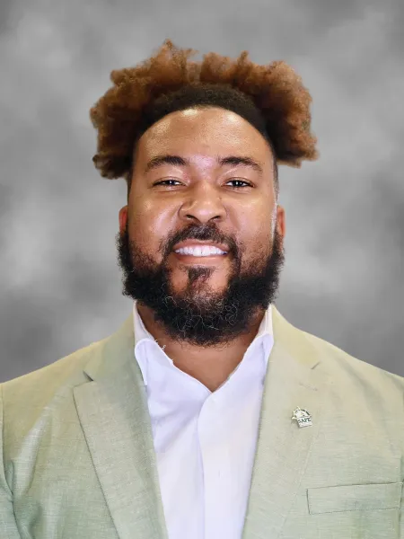 man in green suit jacket smiling against a grey background