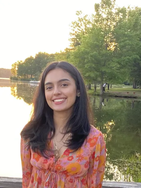 Woman wearing a floral orange top with straight black hair smiling and looking at the camera