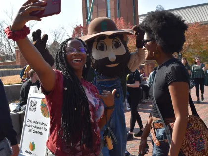 One student taking a selfie with Norm and one student looking at them smiling 