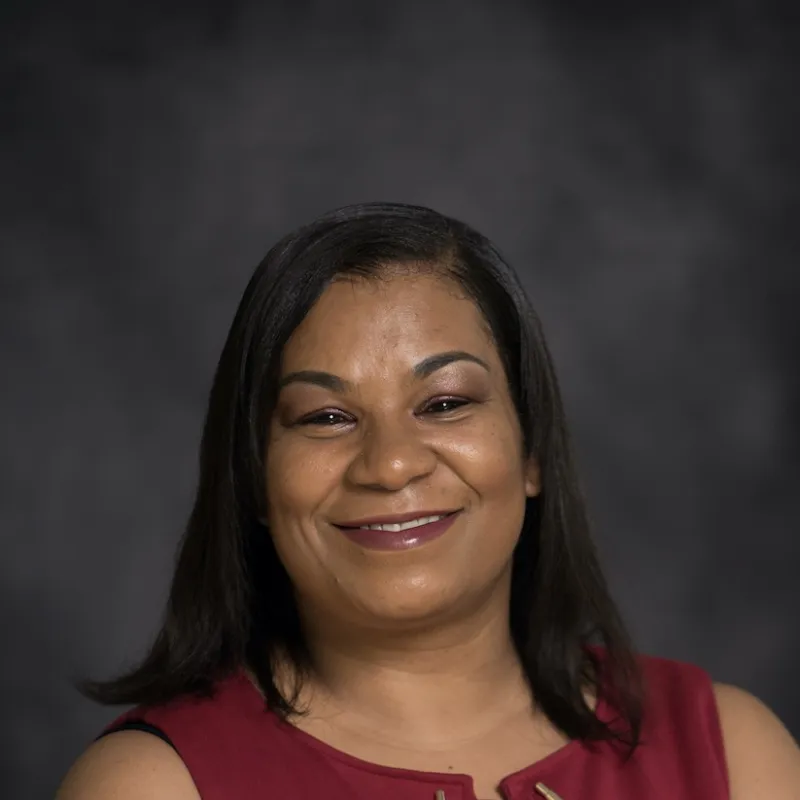 Woman smiling with gray background wearing a red sleeveless shirt 