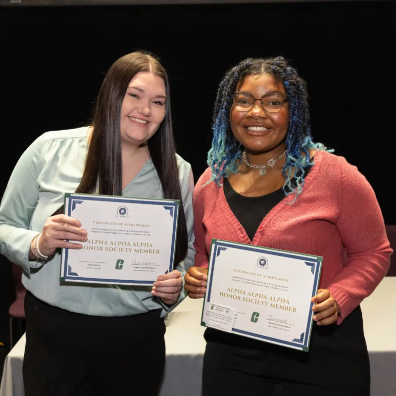 Two students, one wearing a green shirt, and the other wearing a pink blouse. They are both holding a certificate of achievement