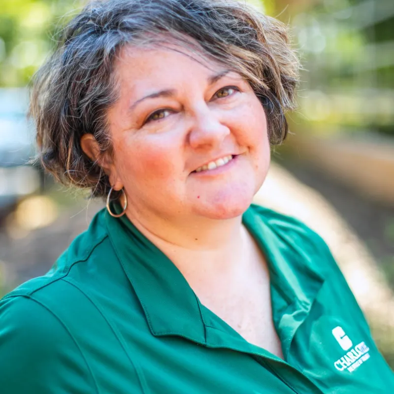 Woman with short hair wearing Charlotte polo smiling and looking at camera from the side