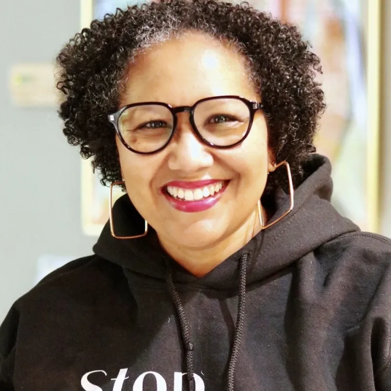 woman wearing black glasses and black sweatshirt with curly black hair and smiling 