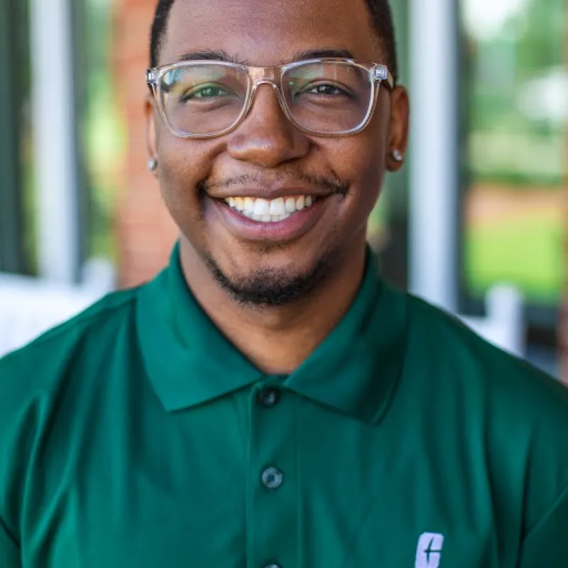 man smiling in a green polo wearing clear glasses with a blurred background