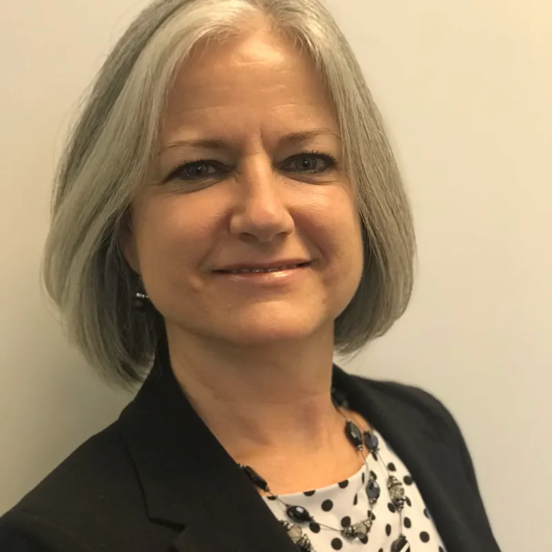 woman wearing polka dot shirt paired with black blazer and smiling to the side