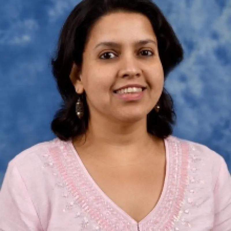Brown woman with short, dark hair smiling and wearing a pink long sleeve top and dangling earrings.