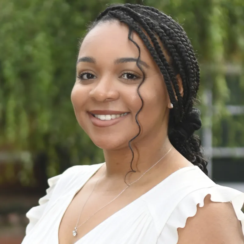 Black woman with braids smiling outside wearing a white blouse. 
