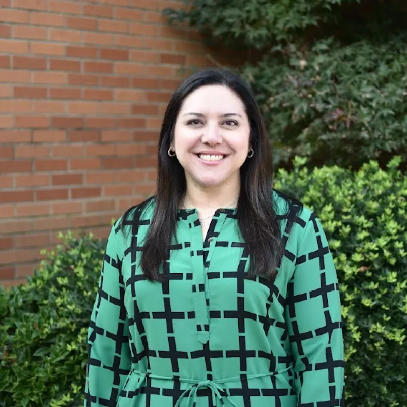 Woman facing the camera smiling with black hair and wearing a green and black shirt. 