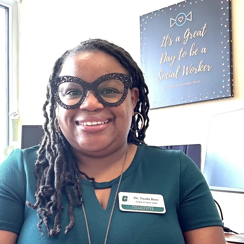Ticola Ross wearing black glasses, a green shirt, smiling with her nametag on