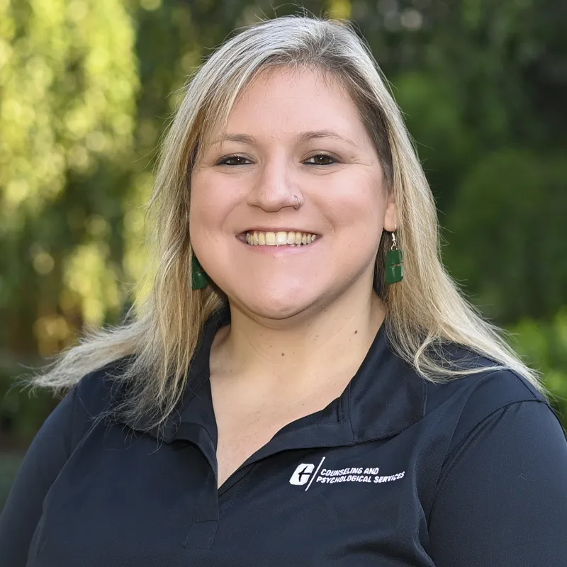 Blonde woman with a black UNC Charlotte polo smiling outside in front of trees