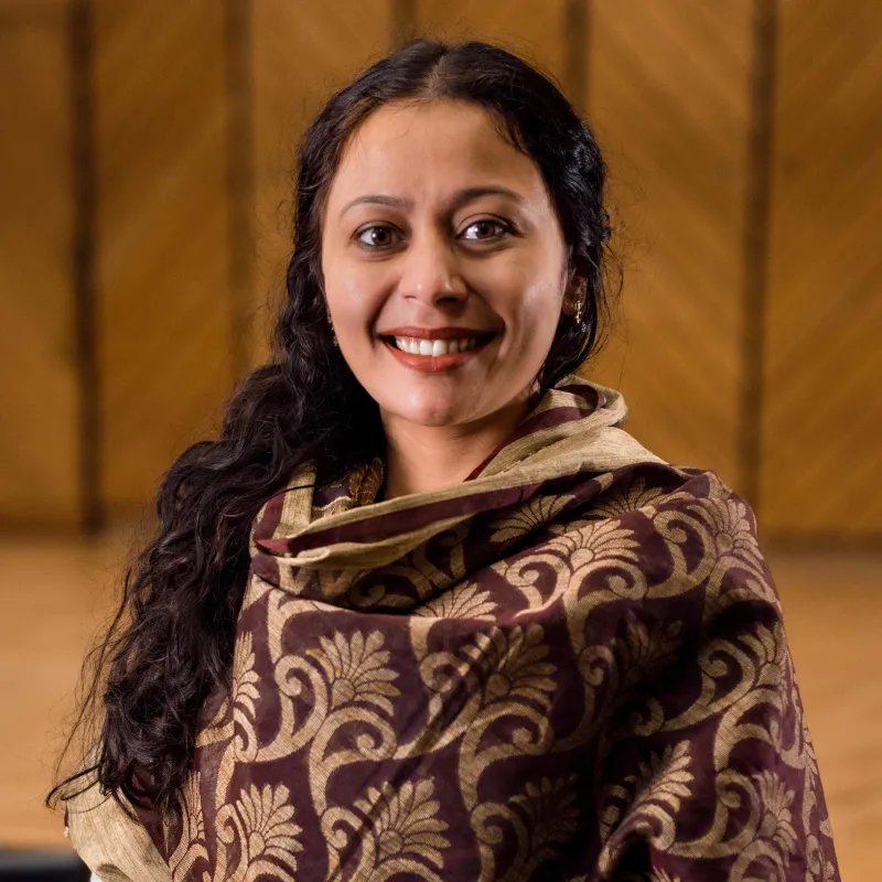 Woman with long, dark hair smiling in front of a background