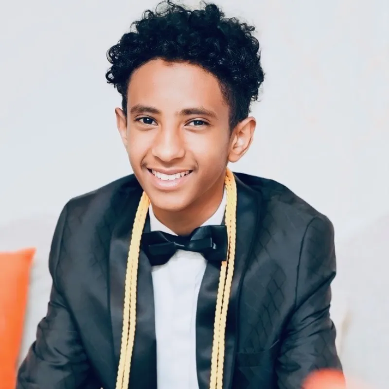 Young man with a tuxedo on and 2 gold graduation cords.