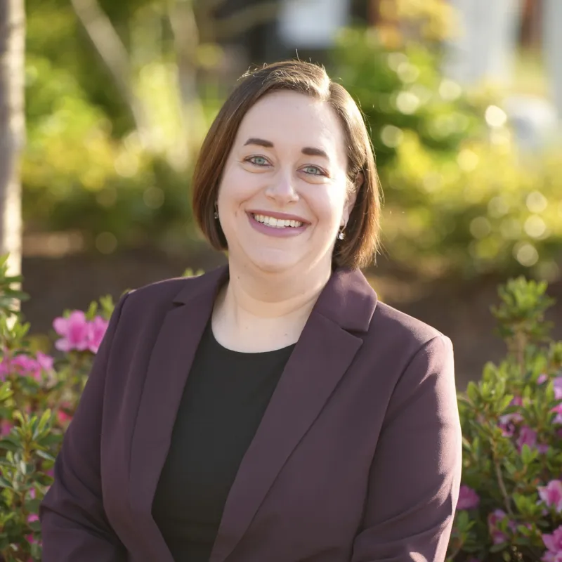 Woman with brown bob cut smiling outside wearing a black shirt and a burgundy blazer