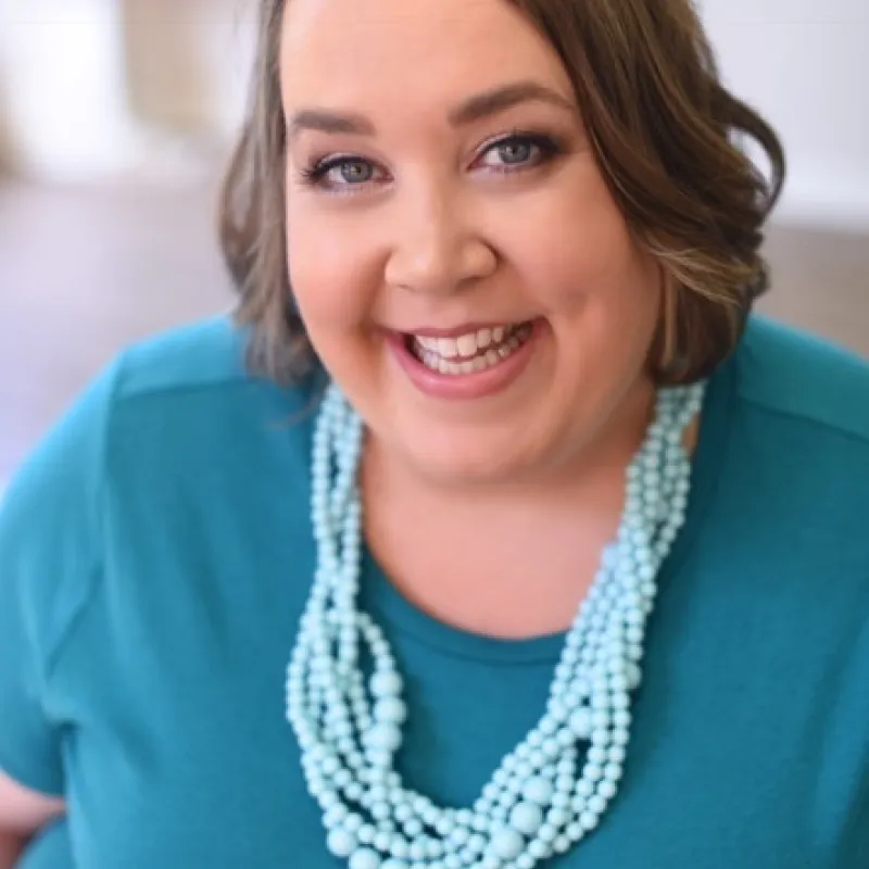 Person in a blue blouse with a blue necklace smiling