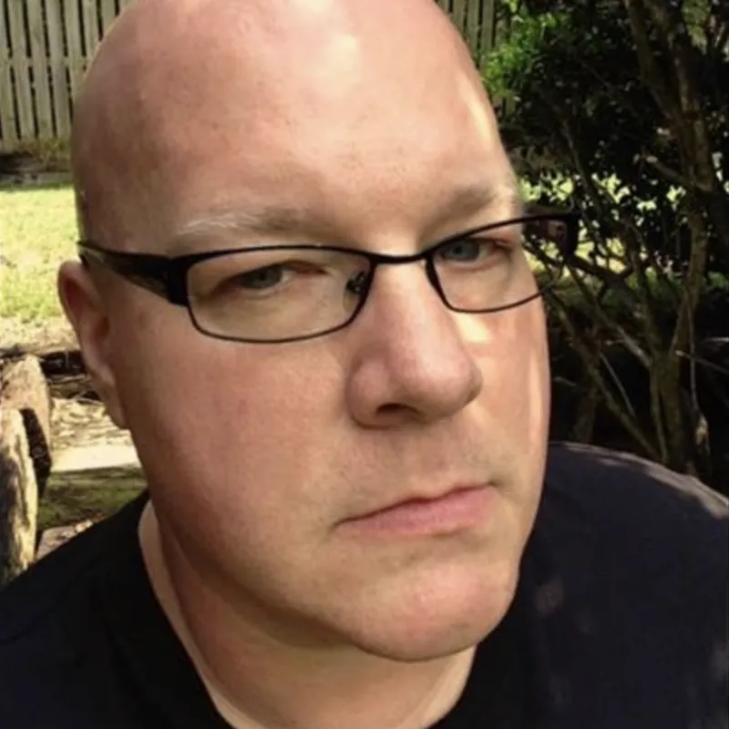 Man wearing square black glasses and black shirt looking at camera
