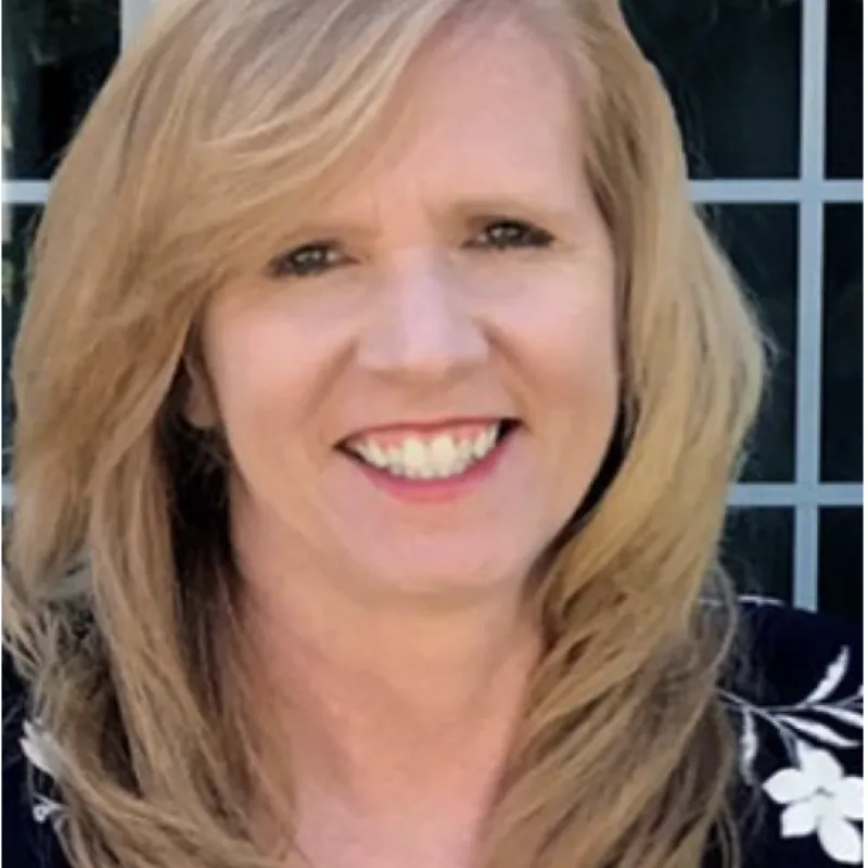 Person smiling directly at camera with blonde curly hair and black floral shirt