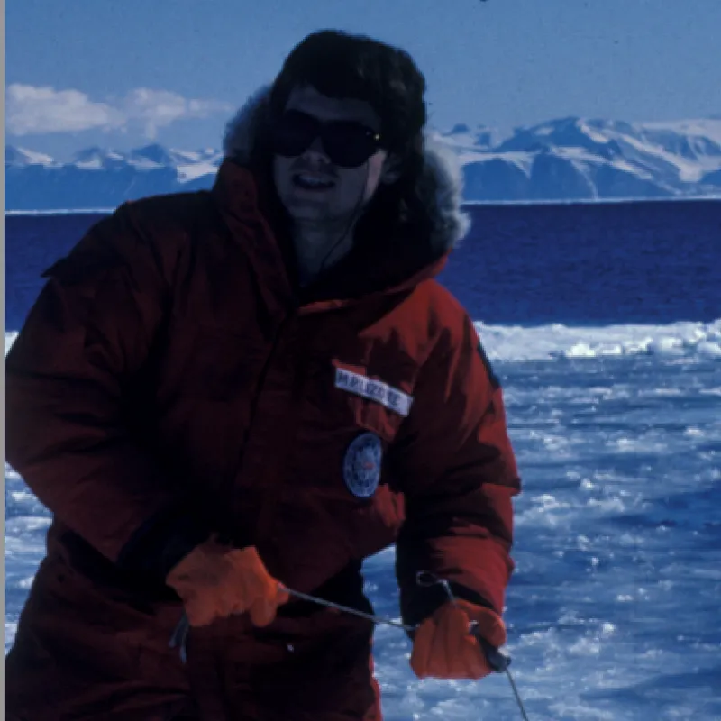 Person wearing a red winter coat and red gloves with sunglasses on, standing with ice all around them.