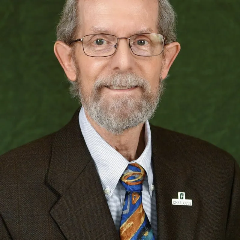 Man with gray hair and beard wearing square glasses and suit with tie