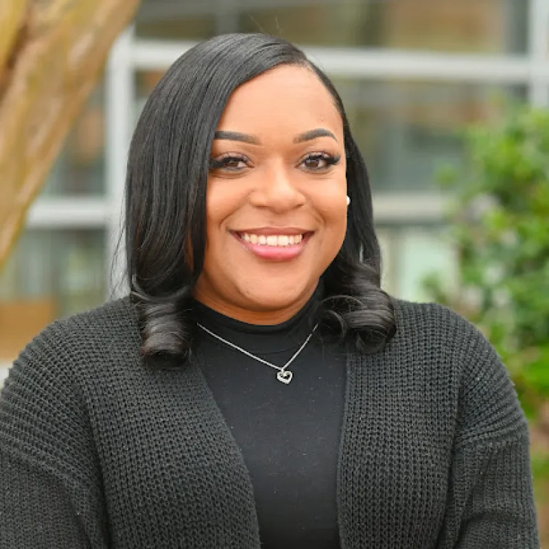 Person with curly black hair wearing black cardigan and shirt 