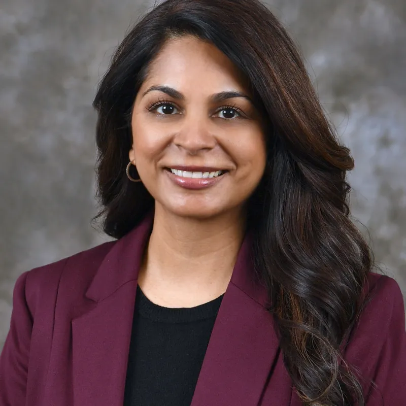 Women wearing dark red blazer paired with black shirt and curled black hair smiling at camera.