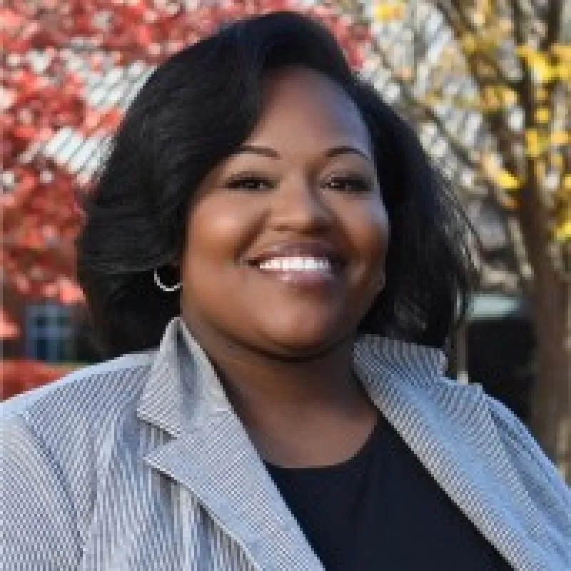 Woman with a black bob smiling outside during fall wearing a black shirt with a gray striped blazer