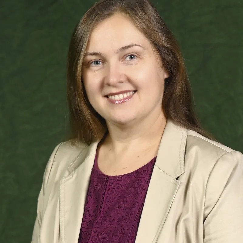 Person with short brown hair smiling sideways to camera wearing beige suit jacket