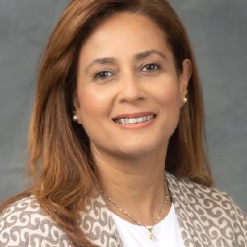 Woman with auburn hair smiling in front of a gray background. 