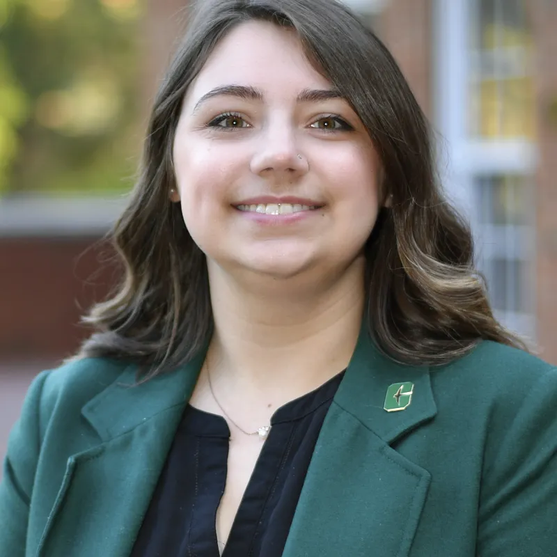 Woman with curly brown hair wearing Charlotte green blazer paired with black shirt and Charlotte pin