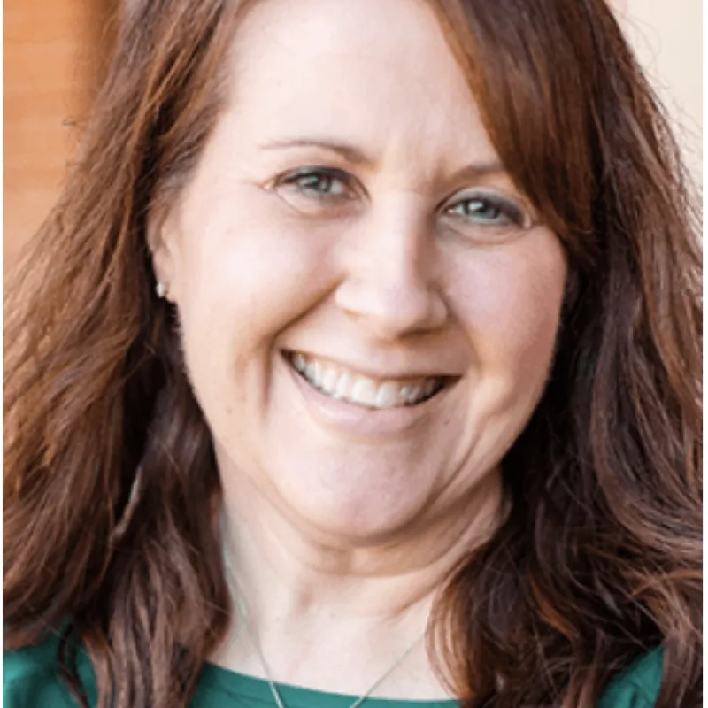 Smiling woman with blue eyes, curled brown hair, and wearing a teal top with a silver necklace